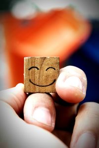 Cropped hand holding wooden block with smiley face