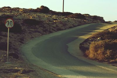Road leading towards mountains against clear sky
