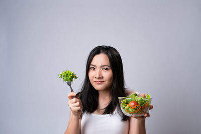 Portrait of woman holding ice cream against white background