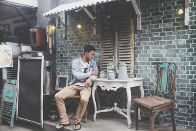 Full length of man sitting by teapots on table