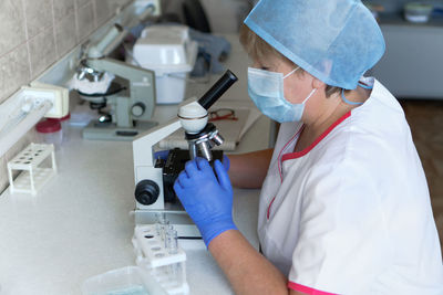 Woman scientist wearing face mask and protective gloves working in laboratory looking 