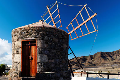 Traditional windmill at by mountains against blue sky