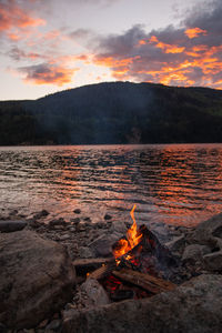 Bonfire on wooden log against sky during sunset