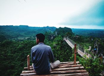 Rear view of man sitting at observation point against sky