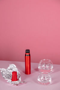 Close-up of containers and bottle on table over pink background