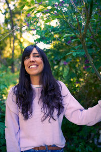 Portrait of smiling young woman standing against trees