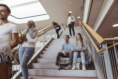 Smiling students sitting on steps while looking at friends in university