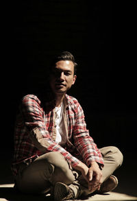 Portrait of a handsome man sitting in a ray of light with a dark background