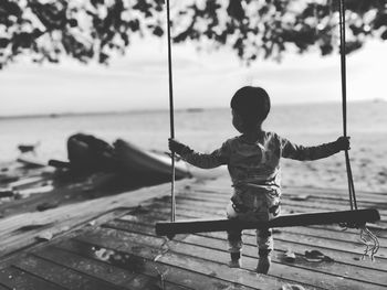 Rear view of boy sitting on swing against sea