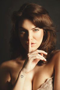 Close-up portrait of young woman with finger on lips against black background