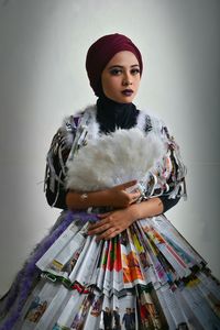 Portrait of young woman wearing newspaper costume against gray background