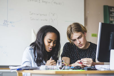 Confident female student preparing science project with young male friend on desk in classroom at high school