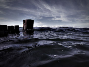 Wooden posts in sea against sky