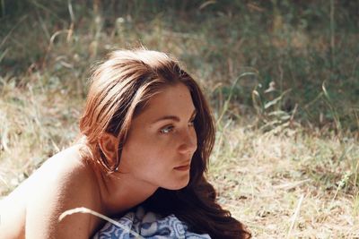 Thoughtful young woman looking away while lying on field