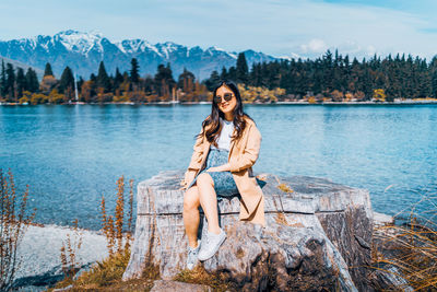 Portrait of young woman sitting on lake against mountains