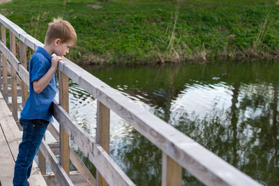Side view of boy standing on bridge over lake