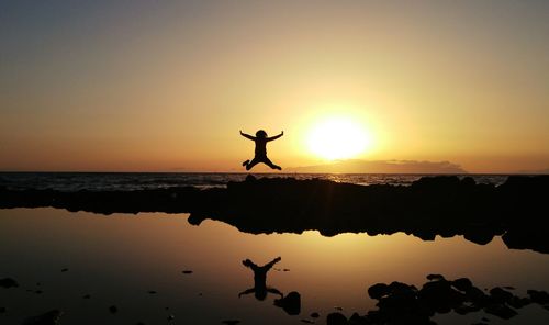 Silhouette man jumping at beach against sky during sunset