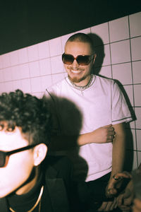 Smiling young man dancing against illuminated white wall at nightclub