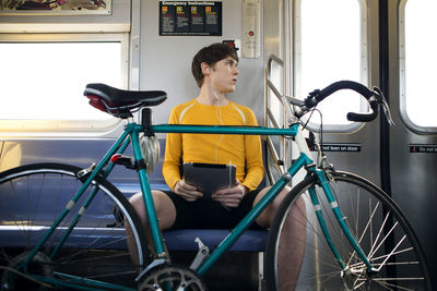 Man holding tablet computer looking away while traveling in train