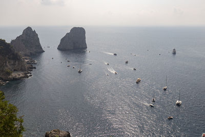 Italy, campania, various boats in front of sea stacks on coast of capri island