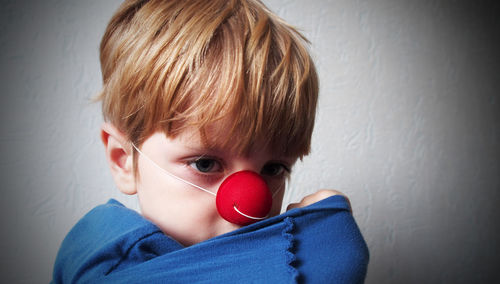 Close-up of boy wearing clown nose against wall