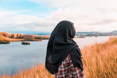 Rear view of woman wearing hijab standing by lake against sky