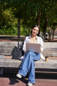 Young woman using laptop while sitting on bench at park