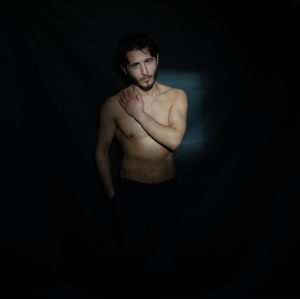 Portrait of shirtless young man standing against wall