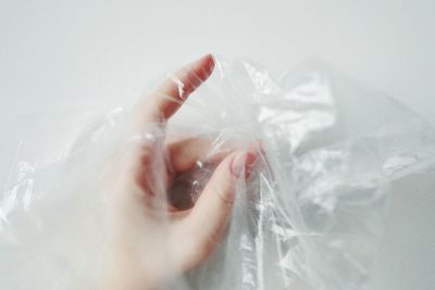 Close-up of woman hand in plastic bag against white background