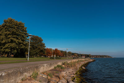 Scenic autumnal view of a promenade along coast of curonian lagoon against clear blue sky