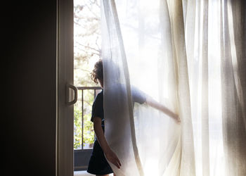Rear view of girl standing by curtains at window