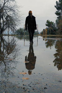 Man walking on puddle over road against sky