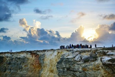 People on rock against sky during sunset