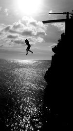 Silhouette woman jumping in sea from cliff