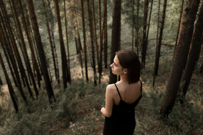 Young woman standing amidst trees in forest