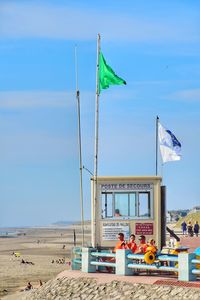 Life guards sitting at beach against blue sky