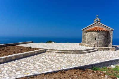 Stone wall by sea against clear blue sky