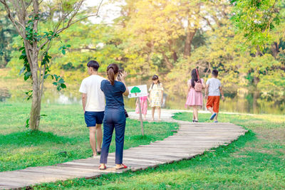 Rear view of woman photographing on pathway while people walking against trees at park