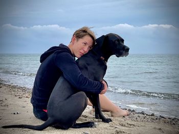 Side view of woman sitting on beach against sky