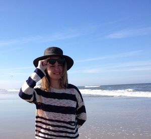 Young woman wearing hat at beach against blue sky