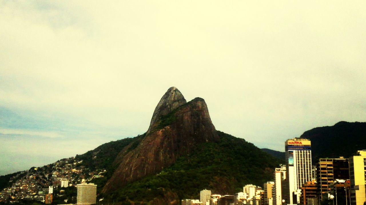 architecture, building exterior, built structure, mountain, sky, city, mountain range, cityscape, cloud - sky, copy space, travel destinations, residential building, outdoors, low angle view, nature, rock - object, day, no people, residential structure, scenics