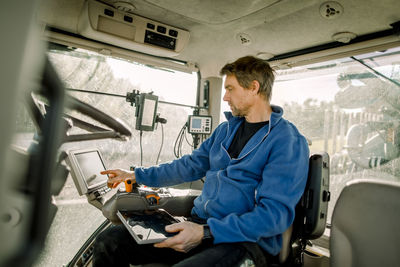 Farmer operating computer sitting in tractor at farm