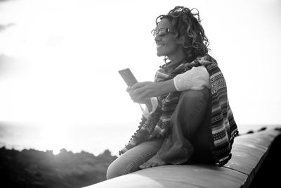 Woman sitting on retaining wall against sky