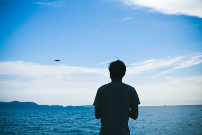 Rear view of man standing by sea against sky