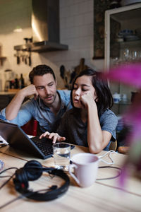 Father looking at son e-learning using laptop on table at home