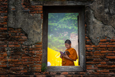 Full length of boy sitting by window against wall