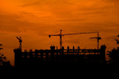 Silhouette cranes at construction site against sky during sunset