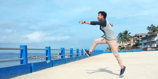 Full length of young man jumping on beach against sky