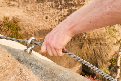 Rock climber's hand hold on steel rope at steel bolt eye anchored in sandstone rock via ferrata.