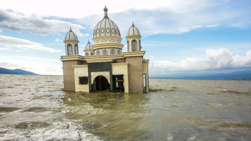 View of building by sea against cloudy sky